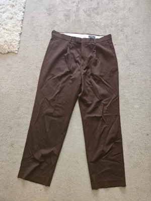 Bruna kostymbyxor från H&M Relaxed Fit - Bruna kostymbyxor från H&M i modellen Relaxed Fit. Byxorna har raka ben, bälteshällor och klassisk kostymlook. Perfekta för en stilren och avslappnad outfit. Materialet känns mjukt och bekvämt mot huden.