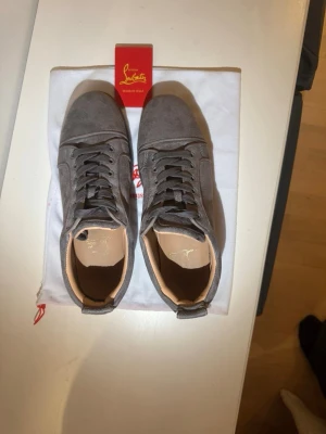 Gråa sneakers från Christian Louboutin - Snygga gråa sneakers från Christian Louboutin i mocka med klassisk snörning och diskret design. Skorna har en mörkgrå sula och ljusbeige innerfoder, perfekt för dig som gillar stilrena och exklusiva sneakers.