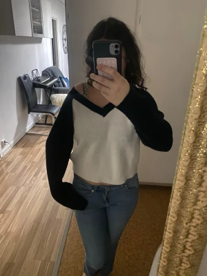 Stickad tröja med V-ringning mörkblå/vit - Säljer en snygg stickad tröja med V-ringning. Knappast använd! Tröjan är vit framtill och baktill med mörkblåa ärmar och runt halsen. Modellen är lite croppad och har långa ärmar. Perfekt för att hålla sig varm och ändå se trendig ut.