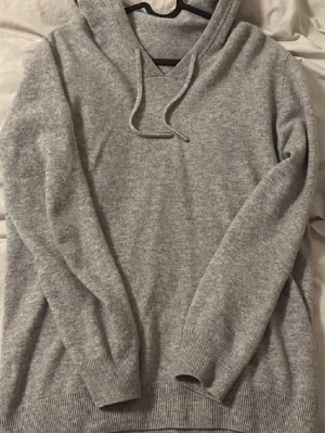 Merinoull hoodie - Mysig grå hoodie i stickad kvalitet med huva och dragsko med metalländar. Tröjan har ribbade muddar vid ärmslut och nederkant, perfekt för en avslappnad och stilren look. Passar dig som gillar enkel och klassisk stil. 8/10 skick 