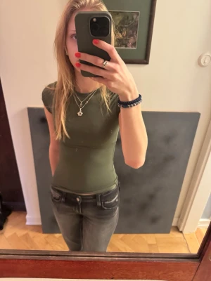 Olivgrön tight t-shirt - Snygg olivgrön t-shirt med tight passform och rund hals. T-shirten har korta ärmar och är tillverkad i ett mjukt, stretchigt material som sitter skönt mot kroppen. Perfekt att matcha med jeans eller kjol för en clean look. Lite som en compression Shirt nästan i träningsaktigt material 