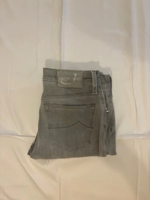 Grå jeans från Jacob Cohen - Snygga grå jeans från Jacob Cohen med klassisk femficksdesign och diskreta sömmar. Jeansen har en rak passform och är tillverkade i mjukt denimtyg med en stilren look. Perfekta för dig som gillar en clean och modern stil. Modellen är 178 cm
