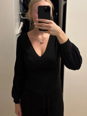 Svart stickad tröja med v-ringning - Snygg svart stickad tröja med djup v-ringning både fram och bak. Tröjan har långa ärmar med lätt puff och ribbade muddar. Perfekt för lager-på-lager och passar till många olika outfits.