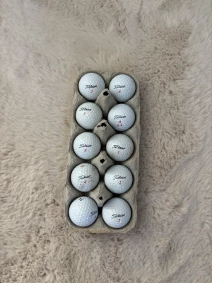 Golfbollar Titleist trufeel - Säljer ett gäng vita golfbollar från Titleist, snyggt placerade i en äggkartong. Perfekt för dig som vill fylla på golfväskan med klassiska bollar. Bollarna har siffror och logga tryckt i rött och svart.