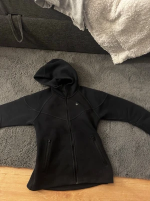 Svart Nike hoodie med dragkedja - Säljer en svart hoodie från Nike med hel dragkedja framtill och två fickor med dragkedja. Hoodien har en stilren design med diskret Nike-logga på bröstet och är tillverkad i ett mjukt och bekvämt material. Perfekt för en sportig och avslappnad look har ej använt .