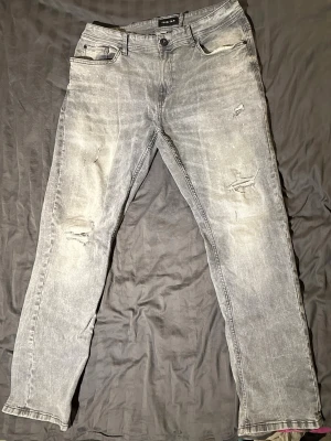 Grå  jeans från smog/denim - Storlek 36/32. Säljer ett par grå jeans från Only & Sons med slitningar och distressed detaljer på benen. Jeansen har fem fickor, knappgylf och raka ben. Materialet är klassisk denim i bomull med en tvättad look och lite färgstänk för extra edge.