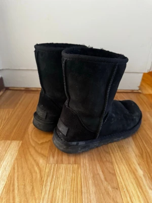 Svarta UGG boots i mocka st 39 - Klassiska svarta UGG boots i mjuk mocka med varmt foder på insidan. Modellen har rund tå och mellanhögt skaft, perfekt för kalla dagar. Tidlös design som passar till det mesta och ger en avslappnad look.