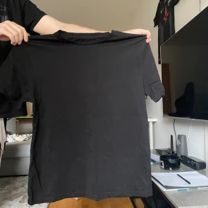 Svart t-shirt med grafiskt tryck - Cool svart t-shirt med färgstarkt grafiskt tryck på ryggen, med texten DAWN och motiv som Frihetsgudinnan och en staty. Trycket har inslag av blått, lila och vitt samt futuristiska detaljer. Klassisk rund hals och korta ärmar, perfekt för dig som gillar streetstyle.