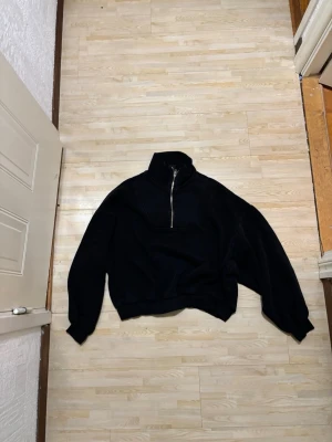 Svart half-zip hoodie - Säljer en svart hoodie med hög krage och half-zip dragkedja framtill. Hoodien har en avslappnad passform och är tillverkad i mjukt sweatshirtmaterial. Perfekt för en chill och stilren look. Har fläckar på sig men märks knappt 