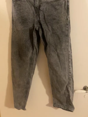 Grå Jeans - Säljer ett par grå  jeans med hög midja och avsmalnande ben. Jeansen har klassisk femficksdesign och är gjorda i denim. Perfekta för en avslappnad och trendig look.