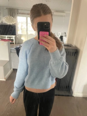 Ljusblå croppad stickad tröja - Mysig ljusblå stickad tröja med croppad passform och långa ärmar. Tröjan har ribbstickade muddar vid hals, ärmslut och nederkant. Den är lite smått nopprig.