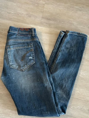 Dondup jeans 30 - Säljer ett par blå jeans med slitningar, färgstänk och trasiga detaljer på benen. Jeansen har en klassisk femficksmodell och raka ben. Materialet är denim och de har en avslappnad, trendig look som passar perfekt till streetwear.