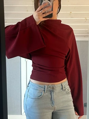 Vinröd topp med vida ärmar - Trendig vinröd topp med breda, långa ärmar och hög hals. Toppen är croppad och har en tight passform i midjan. Använd endast två gånger