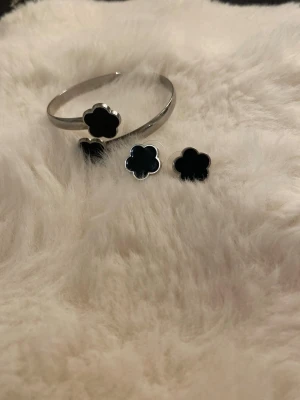 Svarta blomformade örhängen i silver - Snygga örhängen i silverfärgad metall med svart blomformad detalj. De har en stilren och modern look som passar perfekt till dig som gillar minimalistiska accessoarer. Matcha gärna med liknande armband för en komplett stil.