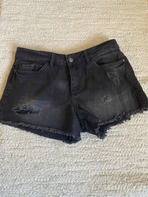 Svarta jeansshorts med slitningar❤️ - Snygga svarta jeansshorts med rå kant och slitna detaljer framtill. Klassisk femficksmodell med knapp och dragkedja. Perfekta för en avslappnad och trendig look.