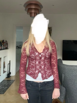 Vinröd spetsblus med v-ringning - Vinröd långärmad blus i spets med v-ringning och figurnära passform. Blusen har fina spetsdetaljer över hela plagget och är något croppad framtill. Perfekt för dig som vill ha en romantisk och trendig look. (Den är i ”M ”men jag skulle säga att den passar för ”S” också 