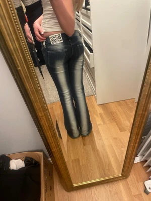 Blå bootcut jeans från weekday - Säljer ett par blå bootcut jeans från Weekday med snygga slitningar och ljus tvätt på framsidan och baksidan. Jeansen har låg midja, klassiska fickor och en cool patch på bakfickan. Perfekta för dig som gillar retrostil och vill ha ett par jeans som sticker ut.