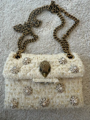 Kurt Geiger beige handväska - En Kurt Geiger handväska som är beige med gulddetaljer. Köpt för 3000kr