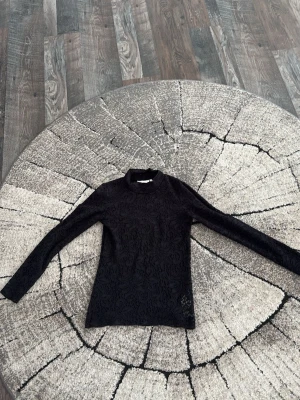 Svart spetsig långärmad polotopp - Säljer en svart långärmad polotopp i spets med snyggt mönster. Toppen är genombruten och har en hög krage som ger en trendig look. Perfekt att styla med jeans eller kjol för en cool outfit. Märket heter inwear.