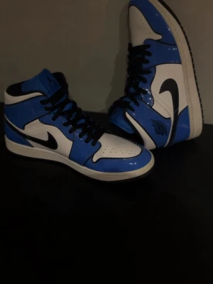 Air Jordan 1 Mid Signal Blue - Air Jordan 1 Mid Signal Blue  med svarta detaljer. Skorna har svart snörning, Ny pris 3500kr
