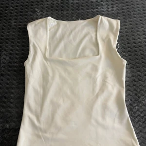 Vit topp från Gina tricot - Säljer en vit stilren topp med fyrkantig ringning och ärmlös design från Gina tricot. I storlek 170.  Det finns en liten sminkfläck, som går bort i tvätten. Tröjan är tillverkad i ett mjukt, stretchigt material. Skriv för fler bilder, frågor eller annat, pris går att diskutera❣️❣️