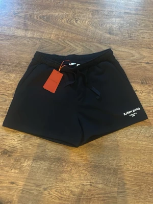 Svarta shorts från Björn Borg - Svarta shorts från Björn Borg med snörning i midjan och diskret logga på vänster ben. Klassisk passform och tillverkade i mjukt material som passar perfekt för träning eller chill. Två sidofickor och elastisk midja för extra komfort.