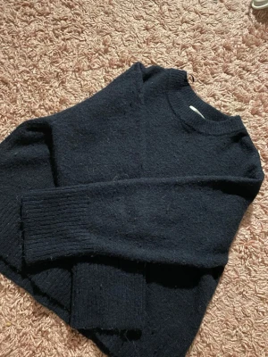 Mörkblå stickad tröja Gina Tricot - Mysig mörkblå stickad tröja från Gina Tricot med rund halsringning och långa ärmar. Tröjan har ribbstickade muddar vid ärmslut och nederkant, perfekt för kyliga dagar. Enkel och stilren design som passar till det mesta.