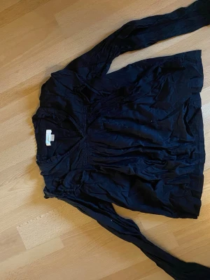 Svart v-ringad blus med lång ärm - Snygg svart blus från H&M med v-ringning och smockdetaljer vid bysten. Blusen har långa ärmar och är tillverkad i ett tunt, mjukt tyg som ger ett avslappnat och flowy intryck. Perfekt att styla med jeans eller kjol. 146/152