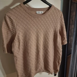Beige quiltad topp från Kappahl - Säljer en beige quiltad topp från Kappahl med korta ärmar och rund halsringning. Toppen har ett diskret rutmönster och är tillverkad i ett mjukt material som känns bekvämt mot huden. Perfekt att styla med jeans eller kjol.