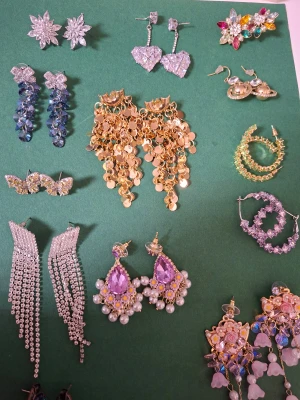Mix av statement örhängen i olika färger fest - Säljer ett gäng unika statement örhängen i olika former och färger. Här finns blommiga, hjärtformade, glittriga och pärlprydda örhängen i silver, guld, lila, rosa, blått och grönt. Perfekt för dig som vill sticka ut med accessoarer som verkligen syns.