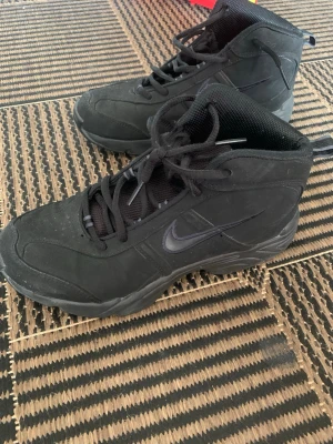 Svarta höga kängor från Nike - Säljer ett par svarta höga kängor från Nike med klassisk swoosh-logga på sidan. Sparsamt användning. 