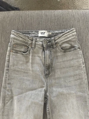 Gråa jeans från 157, XXS Short - Snygga gråa jeans från 157 i storlek XXS Short. Klassisk femficksmodell med hög midja och raka ben. Jeansen har en cool tvättad look och är perfekta för dig som gillar en avslappnad stil. Materialet är mjukt och stretchigt för extra komfort.