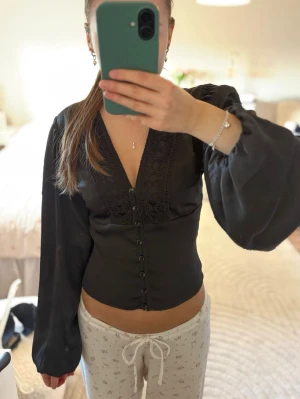Svart blus med spetsdetaljer - Snygg svart blus med spetsdetaljer och knappar, den är endast använd en gång. Så i superbra skick!🩷🩷 slutsåld och finns inte att köpa ny💐