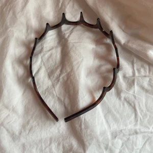 Brunt diadem med taggig design - Säljer ett brunt diadem i plast med cool taggig form och sköldpaddsmönster. Perfekt för dig som vill ha en edgy accessoar som sticker ut och håller håret på plats. Passar till alla outfits där du vill addera lite attityd. 