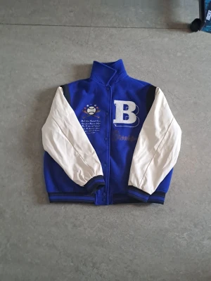 bomberjacka med B-tryck - Snygg blå bomberjacka med vita ärmar och stora bokstaven B på bröstet. 