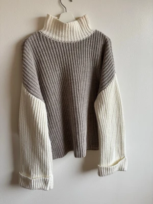 Beige och vit stickad tröja NA-KD - Säljer en chunky stickad tröja från NA-KD i beige och vitt. Tröjan har hög krage, breda ärmar med uppvik och kontrastfärgade partier. Samt slits på sidorna. Perfekt för kalla dagar och riktigt snygg till jeans eller kjol. Smink fläck på kragen som säkert går att tvätta ur!