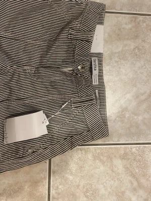 Randiga jeans från Bershka - Snygga svartvit-randiga jeans från Bershka med raka ben och hög midja. Jeansen har klassiska fickor fram och bak samt bälteshällor. Materialet är bomull och de har en avslappnad passform som ger en cool streetstyle-vibe.