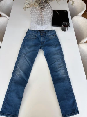 Blå slim fit jeans från Replay - Snygga blå slim fit jeans från Replay med klassisk femficksdesign och lätt slitna detaljer. Jeansen har normal midja och är tillverkade i mjuk denim som ger en bekväm passform. Perfekta för en trendig och avslappnad stil.