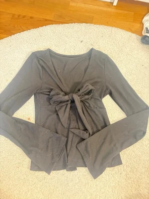 Svart långärmad topp med knyt - Snygg svart långärmad topp med stor knytning framtill som ger en unik look. Toppen har en figurnära passform och är tillverkad i mjukt bomullsmaterial. Perfekt för dig som vill ha något stilrent men ändå med en twist. Lappen är bortklippt men den är från Gina tricot i storlek s. 