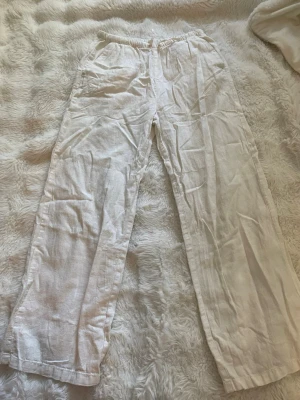 Vita linnebyxor från H&M - Säljer ett par vita linnebyxor från H&M i storlek 146. Byxorna har resår i midjan och raka ben, tillverkade i ett luftigt linnematerial. Perfekta för en avslappnad och stilren look.