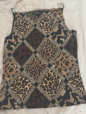 Leopardmönstrad linnetopp med smala band - Cool linnetopp med leopardmönster i beige, brunt och svart. Toppen har smala axelband och ett rutigt patchwork-inspirerat mönster med olika djurprints. Skön att ha på stranden. Köpt i Thailand 