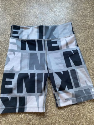 Nike gråmönstrade träningstights shorts - Säljer ett par grå och svarta träningstights shorts från Nike i storlek 137-146 cm. Är knappt använda. Är dock en liten fläck på sidan som knappt syns. Se bild 2. Nikelogan på sidan har också spruckit lite. Väldigt sköna!