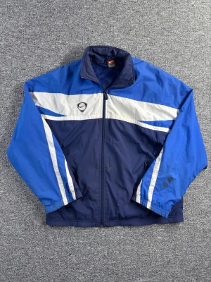Vintage Nike Windbreaker – Size S - Vintage windbreaker från Nike i klassisk blå färgblock design. Lätt jacka perfekt för både sport, streetwear och vardagsbruk. Retro 90s / Y2K vibe.  📏 Storlek: S 📐 Mått visas i bilderna ✨ Skick: Använd – fläckar finns och visas tydligt i bilderna  Perfekt som lätt jacka till vår/sommar eller för en vintage streetwear outfit.  💸 Följ mig så får du 10% rabatt på köpet!   