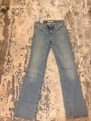 Ljusblå bootcut jeans från Levis - Säljer ett par ljusblå bootcut jeans från Levis med klassisk femficksdesign och råa kanter nertill. Jeansen har en något utsvängd passform och normal midja. Perfekta för en avslappnad och trendig look.
