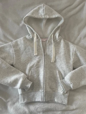 Ljusgrå zip hoodie från Gina Tricot - Mysig ljusgrå hoodie från Gina Tricot med dragkedja framtill, stor huva och vita dragsnören. Aldrig använd