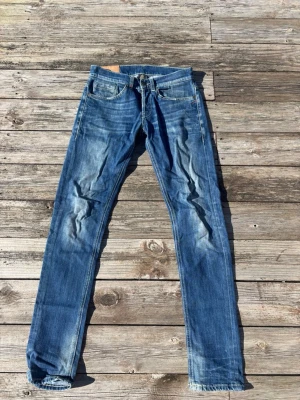 Blå dondup jeans med slitningar - Säljer ett par blå slim fit jeans med snygga slitningar och tvättade detaljer på benen. Klassisk femficksmodell med dragkedja och knapp i midjan. Jeansen har kontrastsömmar och är tillverkade i bomull med lite stretch för skön passform. Strl 30