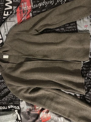 Grå ziptröja i ullmix - Snygg grå ziptröja med minimalistisk design och rak passform. Tröjan har dragkedja framtill, ribbade muddar och är tillverkad i en mjuk ullmix som känns skön mot huden. Perfekt för lager på lager och enkel att matcha med olika outfits.