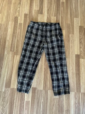 Rutiga pyjamasbyxor i svart, grått och vitt - Mysiga pyjamasbyxor med svartvitt rutmönster och elastisk midja. Perfekta för chillkvällar hemma. Tillverkade i mjukt tyg som känns skönt mot huden. Klassisk rak passform och avslappnad stil.