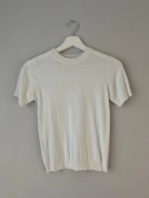 Vit kortärmad stickad topp - En enkel och stilren vit stickad topp med korta ärmar och rund hals. Perfekt att matcha med jeans eller kjol för en clean look. Mjuk och bekväm, passar till många olika outfits.