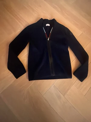 Mörkblå ziptröja från Moncler - Snygg mörkblå ziptröja från Moncler med hög krage och hel dragkedja framtill. Tröjan har en stilren design och är tillverkad i ett mjukt, stickat material som passar perfekt till lager på lager. Klassisk och tidlös modell. Barn storlek. 12 år/ 160 cm